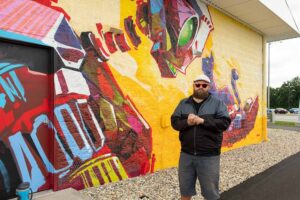 artist dan thompson standing in front of his mural at jiffy lube